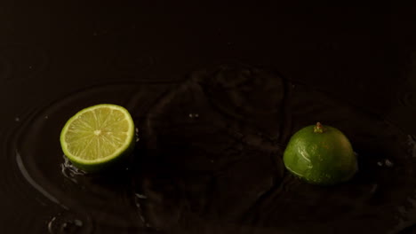 Lime-halves-dropping-on-wet-black-surface