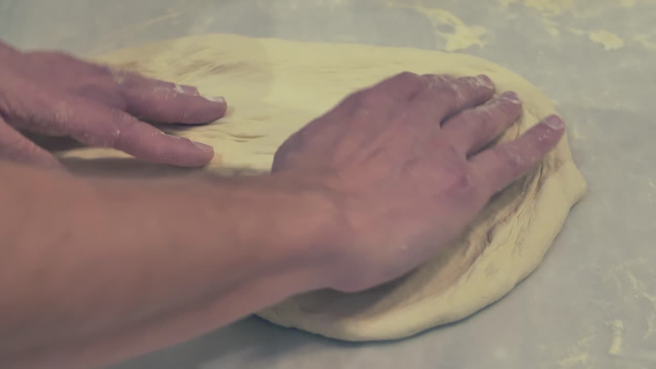 итальянский повар растягивает и разворачивает тесто для пиццы на столе голыми руками