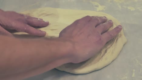 Italienischer-Koch-Streckt-Und-Dreht-Den-Pizzateig-Auf-Dem-Tisch-Mit-Bloßen-Händen