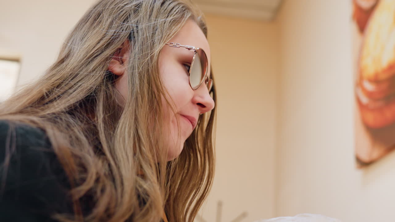 Blanke vrouw met bril die binnenshuis een hap neemt van een deegbal, nylon verpakking bij haar mond houdt, zachte binnenverlichting benadrukt kalme beweging en alledaags moment met een warme realistische sfeer