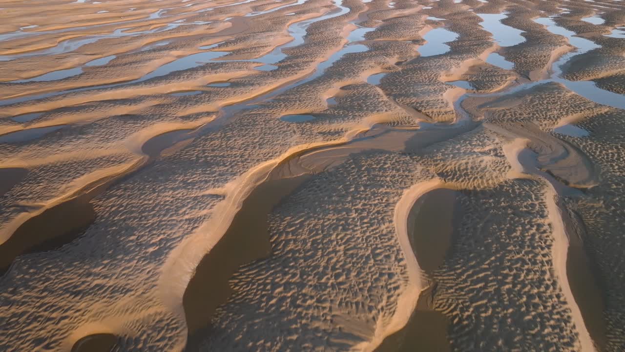 Tidal sand ripples catching setting sun colour with reflecting seawater pools.