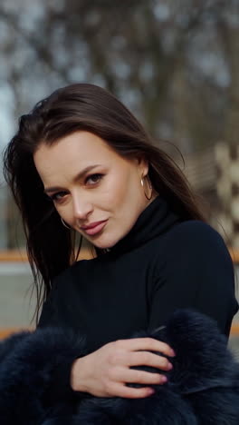 portrait of beautiful model. glamour girl in black fur coat posing on camera outdoors. attractive brunette in the park. camera moves around. vertical video