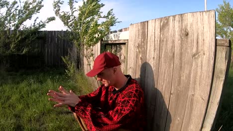 male adult against a fence in the wind looking into the sunny wearing a black and red sweater