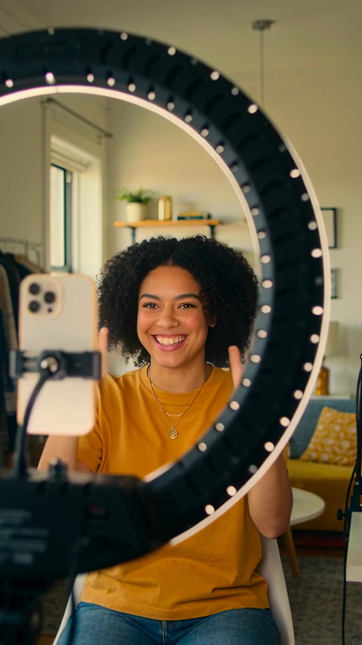 Video verticale: Donna con top giallo che si sistema i capelli guardando il telefono, filmando a casa con una ring light.
