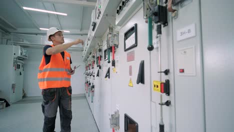 el ingeniero eléctrico que trabaja comprueba la tensión de corriente eléctrica y la sobrecarga en la parte delantera del gabinete del centro de carga o de la unidad de consumo para el mantenimiento en la sala principal del sistema de distribución de energía.