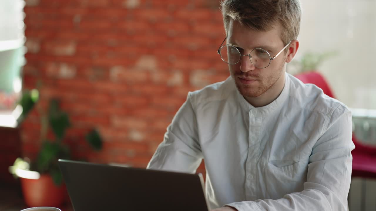 hombre guapo está escribiendo mensajes y enviando en chat en línea en la computadora portátil, sentado y trabajando en una cafetería
