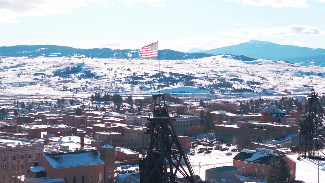 Riprese drone sopra Butte, Montana, che inquadrano una struttura commemorativa con una bandiera americana che sventola sullo sfondo di un paesaggio urbano invernale innevato e delle colline ondulate circostanti