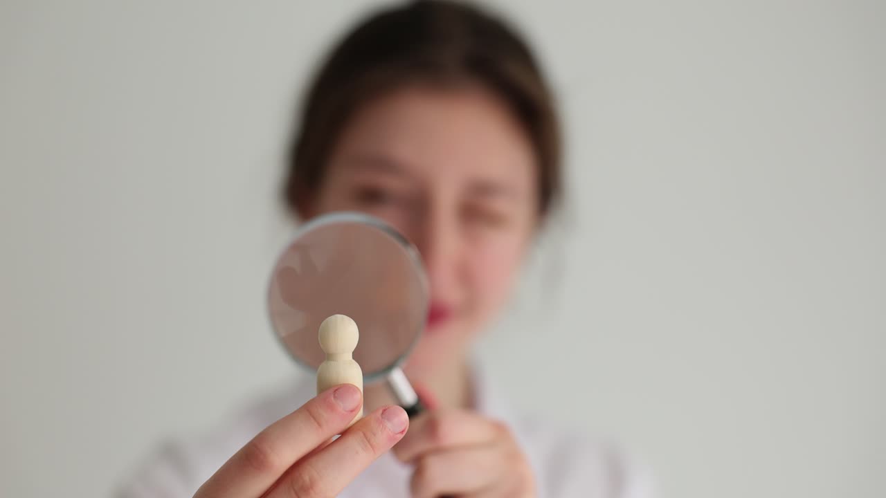 Woman Examining Small Wooden Human Figure with Magnifying Glass