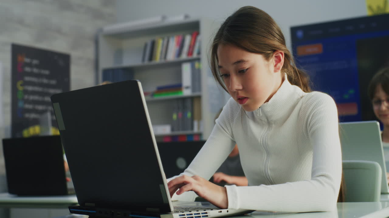 Young asian girl smiles using laptop computer in elementary school classroom