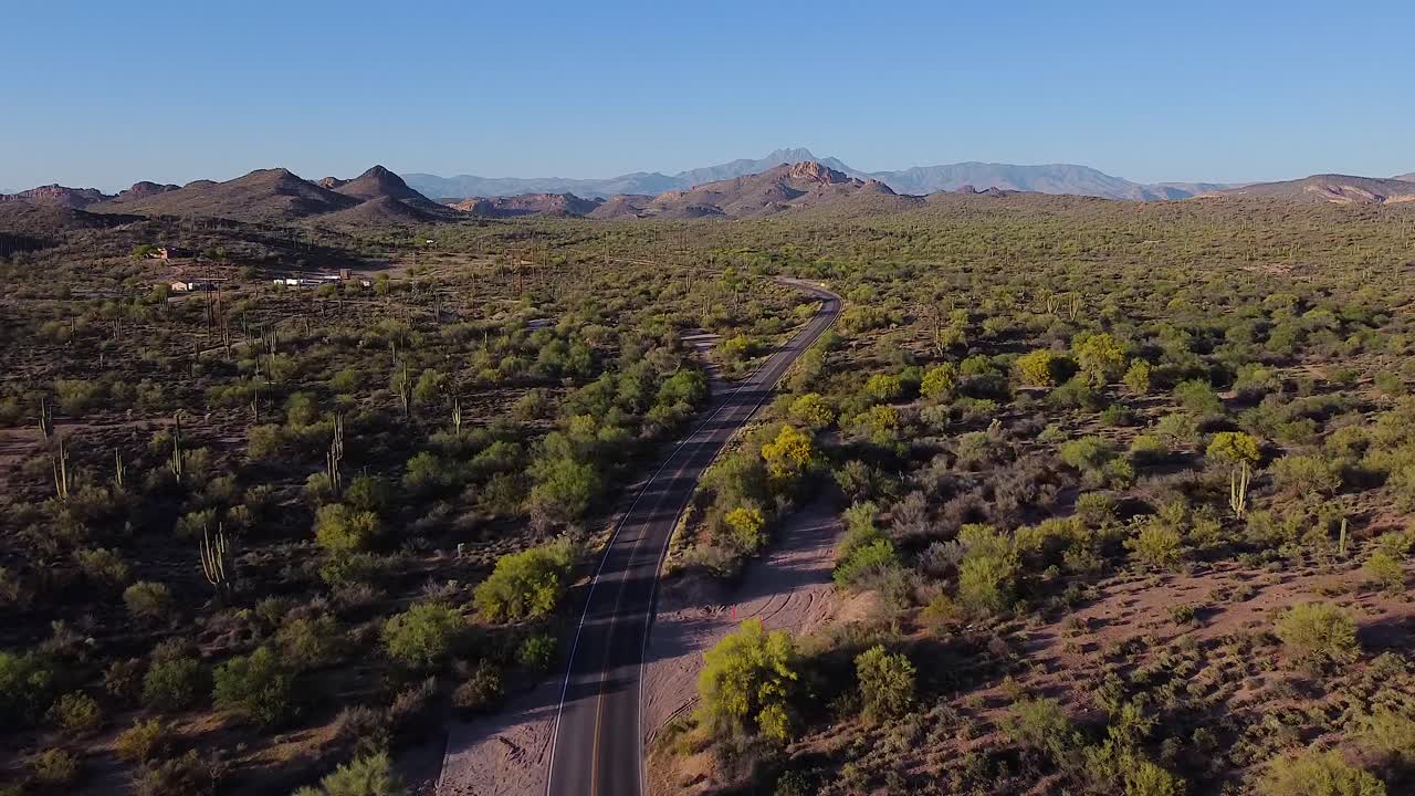 해가 지는 동안 티와 산과 함께 로드 트립을 위해 사막의 긴 휘어지는 도로