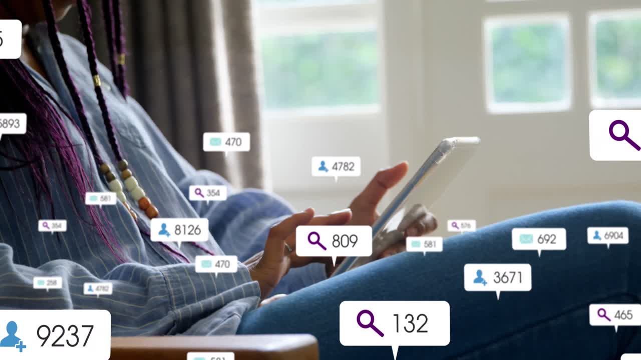 Animation of social media icons floating over mid section of a woman using digital tablet at home