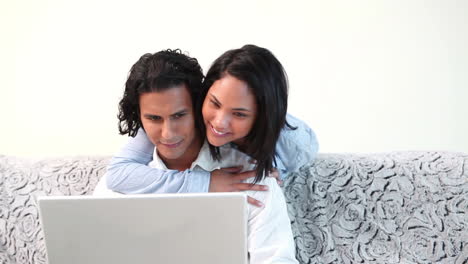 mujer abrazando a su novio que está usando la computadora portátil en el sofá