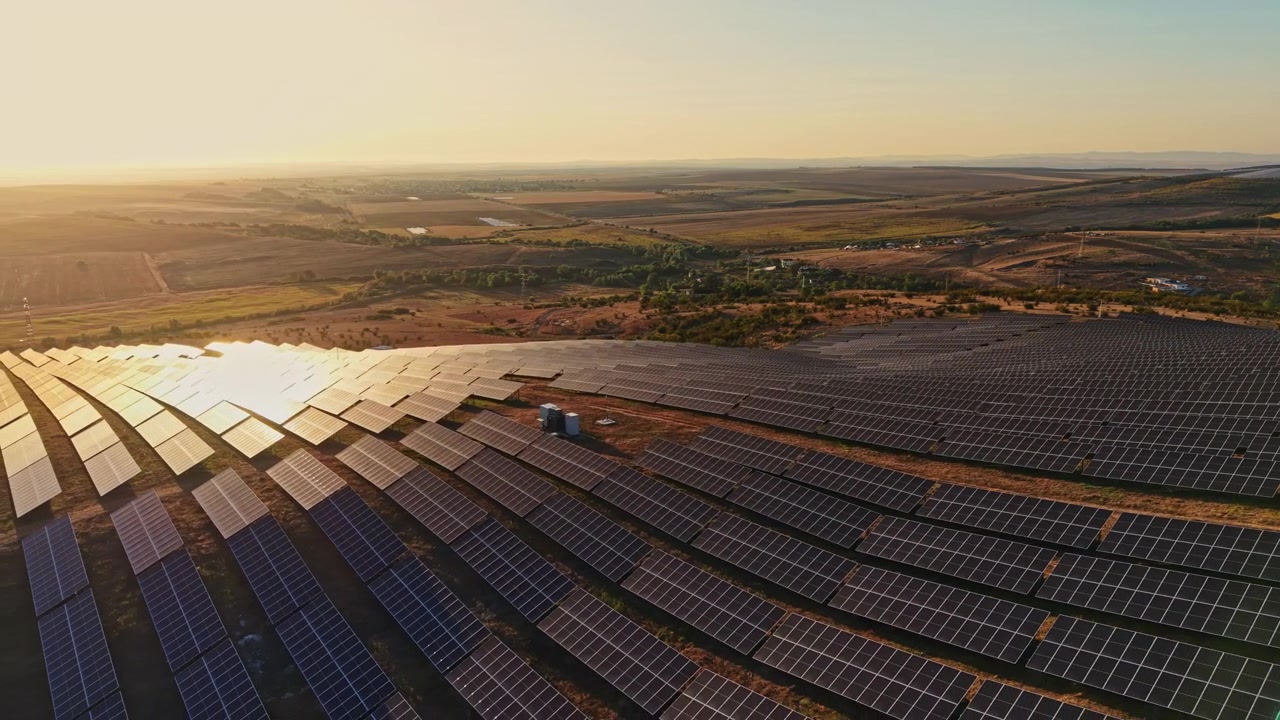 Solpaneler dækker et stort område på en bakkeskråning ved solnedgang, med marker og bakker synlige i det fjerne