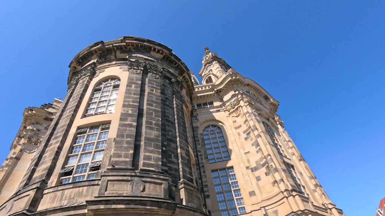Low-angle upward pan of ornate Baroque church facade in bright daylight against clear blue sky