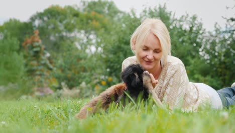 woman playing with two puppies, lying on the lawn in her backyard