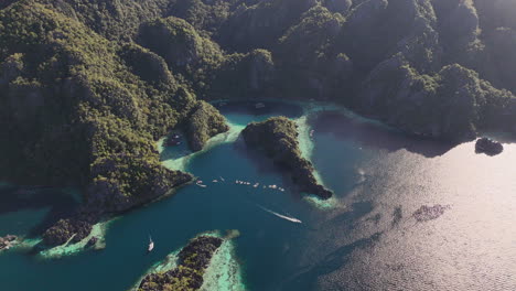 drone footage of coron island, philippines, revealing its breathtaking beaches, lush vegetation, and towering rock formations. with a boat anchored in the water.