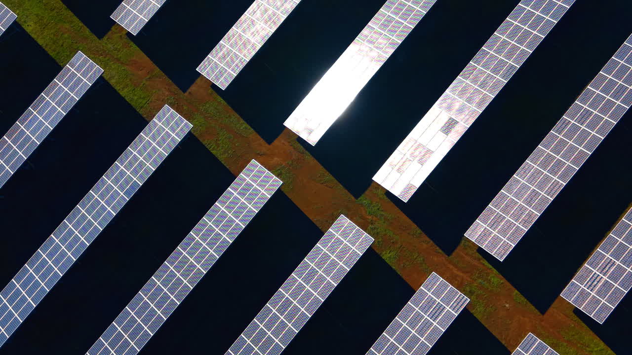 Veduta aerea dall'alto di pannelli solari fotovoltaici in file. Ripresa da drone dall'alto di schiere di pannelli solari su terreno scuro con chiazze d'erba verde.