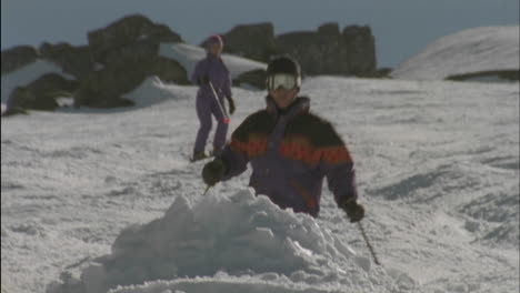 three people are skiing one jumps over a mound of snow