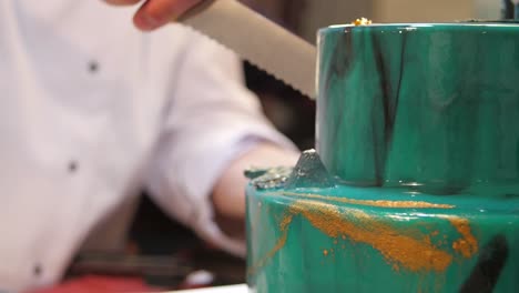 chef cutting a beautiful turquoise and gold marbled cake