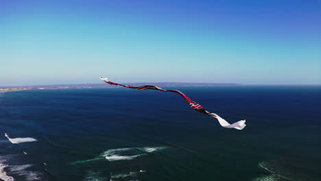 Traditional-balinese-kite-with-long-flowing-tail-flying-high-above-sea