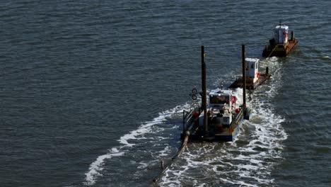 an aerial view of two tugboats, and a small barge dredging a bay on long island, new york on a sunny day