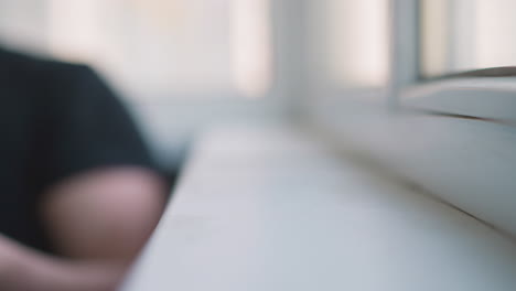 Man-hand-takes-mobile-phone-from-white-windowsill-in-room