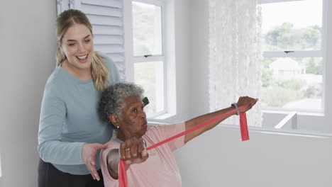 Caucasian-nurse-with-senior-woman-exercising-with-rubber-band,-copy-space,-slow-motion