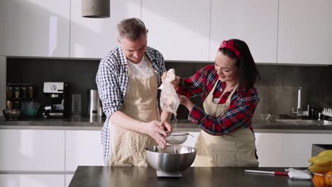 Portrait-of-a-couple-sifting-flour-to-make-bread-in-kitchen