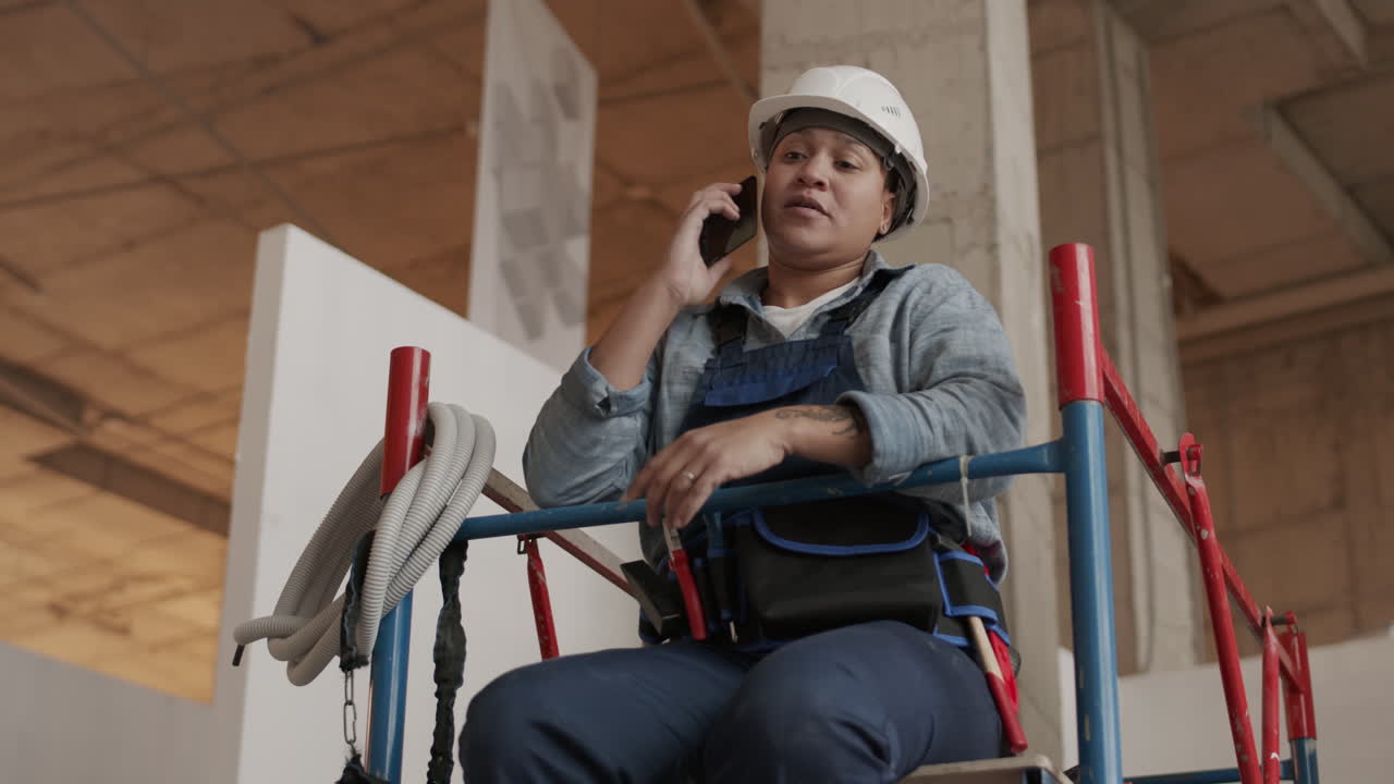 trabajador sentado en el andamio usando un teléfono inteligente