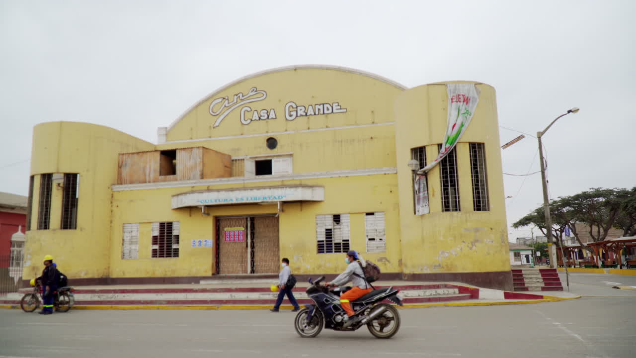 Transportation and People Outside the Casa Grande, Ascope, La Libertad, Peru. Sliding Pan Shot Along Road Outside Entrance of an Old Abandoned Cinema Building