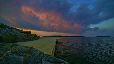 colorful sunset cloudscape over a lake or fjord with a wooden dock in the rocky foreground - sliding time lapse