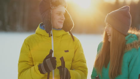 A man embraces a woman standing in the woods at sunset after a winter walk on skis. St. Valentine&#039;s Day. Romance and warm feelings of lovers. Slow motion