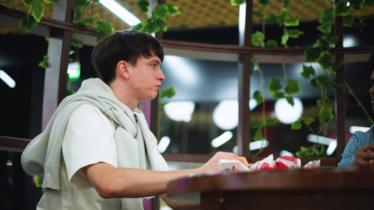 white young man with friend near dazzling flower bulbs in cafeteria, background filled with vibrant artificial blooms and soft light, candid portrait capturing admiration of floral display