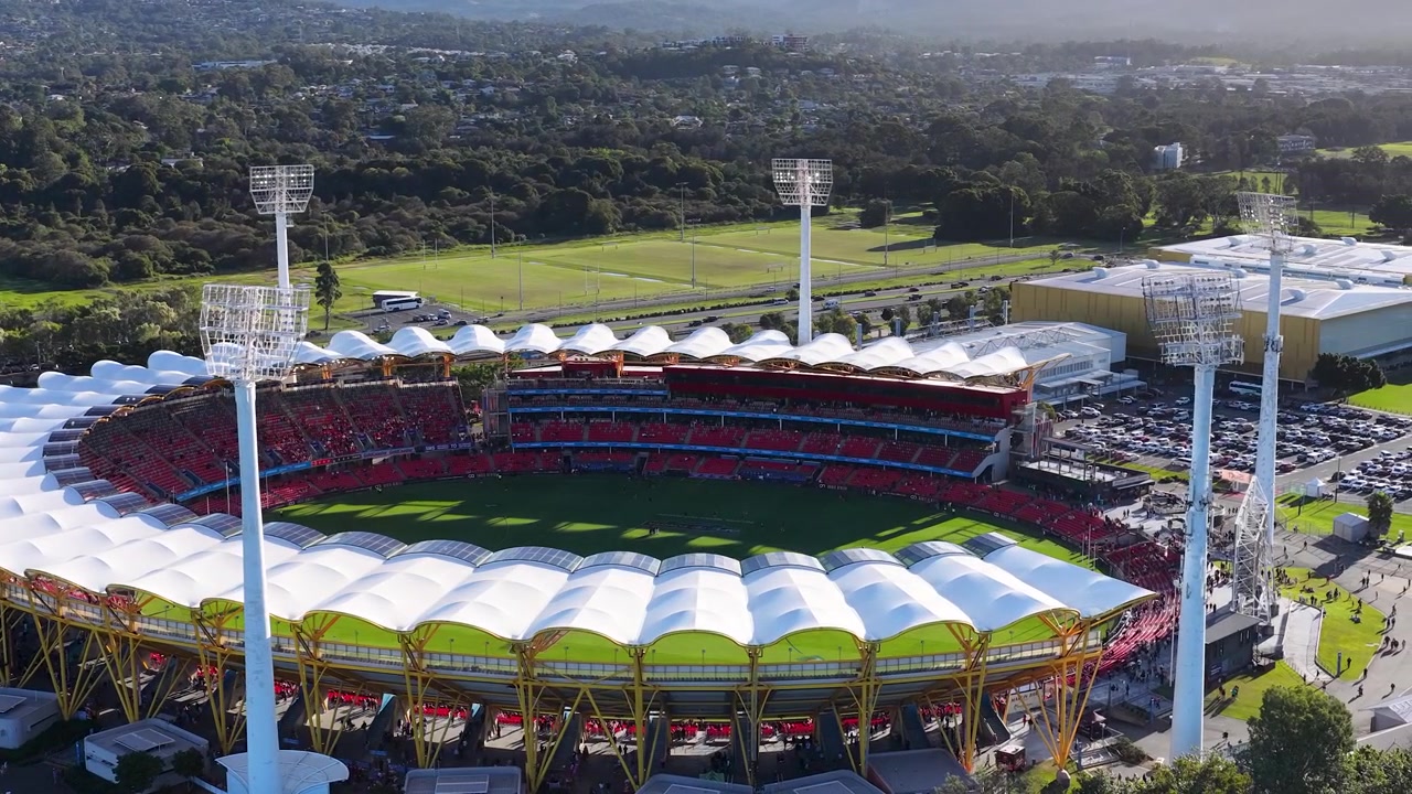 High-angle drone shot captures a large circular sports arena under bright sunny daylight conditions.