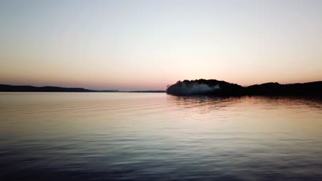 un lago pacífico al atardecer, reflejando los suaves colores pastel del cielo con una pequeña silueta de isla en la distancia