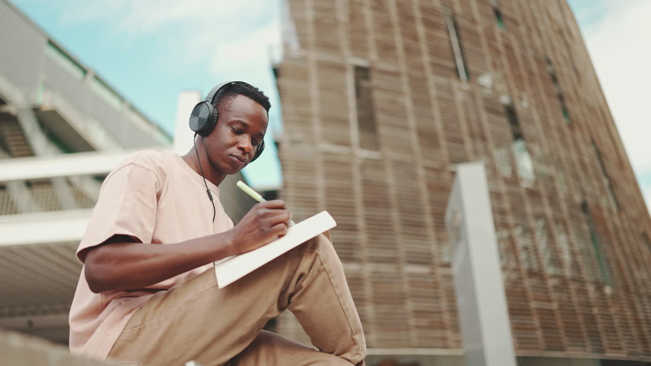 Man with headphones writing in notebook in urban setting