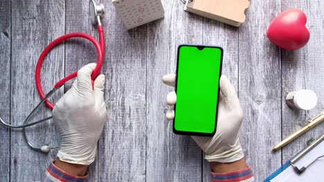 mano del médico sosteniendo un teléfono inteligente con pantalla en blanco en el escritorio de la clínica