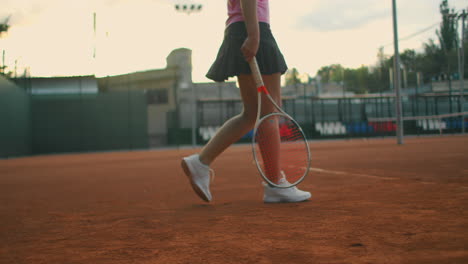 at tennis practice the girl approaches the central service line and prepares to serve knocks the ball several times on the ground and catches the ball with her hand. long shot at ground level