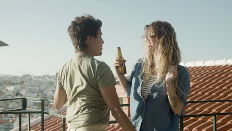 cheerful couple holding beer and dancing at rooftop party