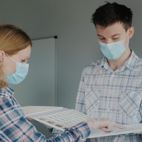 the designer shows samples of materials to the customer - both wear protective masks