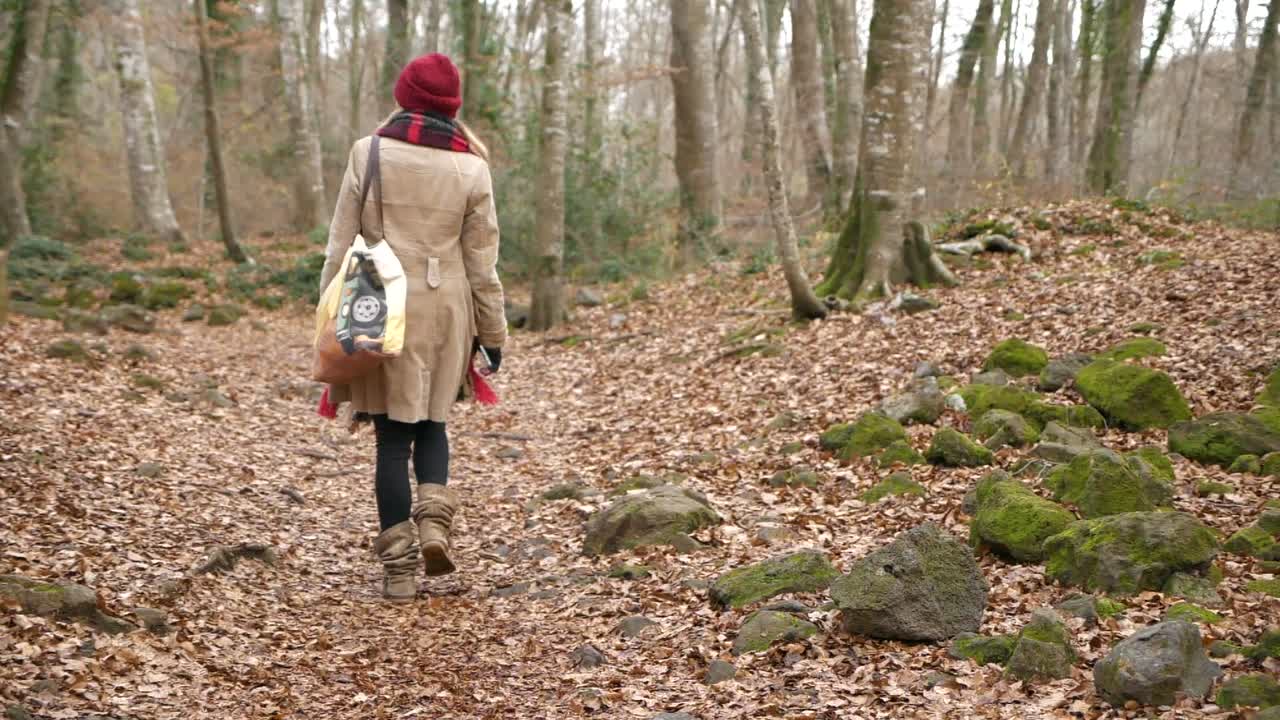 Kvinde set bagfra, der går alene i bøgeskov om vinteren.