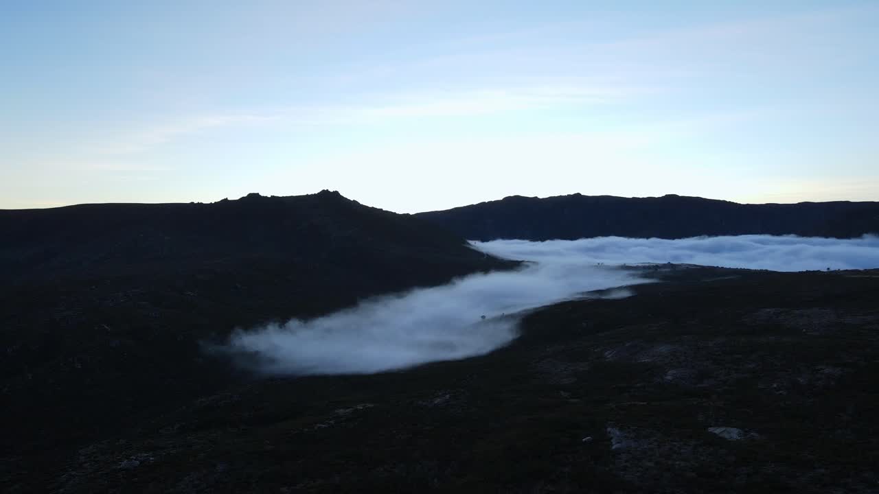 Aerial far away view of a valley covered with fog and clouds drifting away