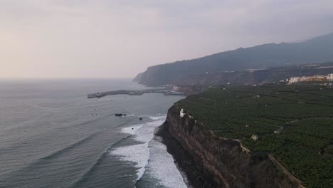 Aerial-forward-along-cliffs-of-banana-plantation-fields-and-Tazacorte-harbor-in-background,-La-Palma-island