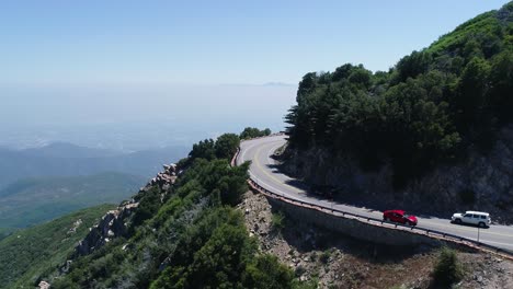 Eine-4K-Tracking-Drohnenaufnahme-Von-Autos,-Die-Auf-Einer-Straße-Fahren,-Die-Hoch-Oben-Auf-Einem-Gebirgspass-In-Der-Nähe-Des-Angeles-National-Forest-Und-Des-Berges-Gefunden-Wurde