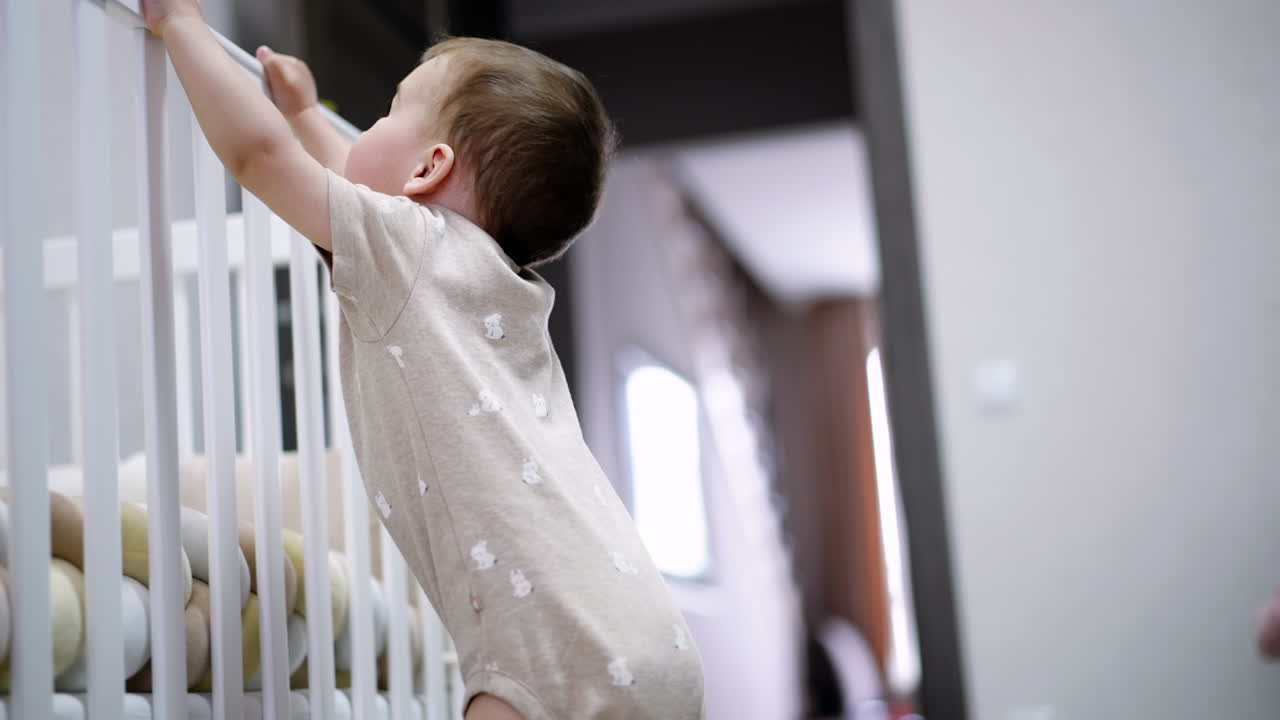 Un bambino piccolo scuote la culla con eccitazione. Il bambino gioca nella sua stanza. Vista dal basso.