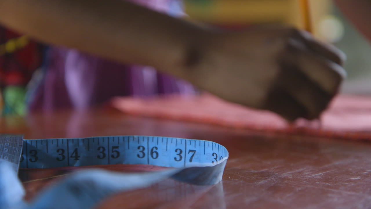 A woman seamstress drawing on a piece of cloth next to a tape measure