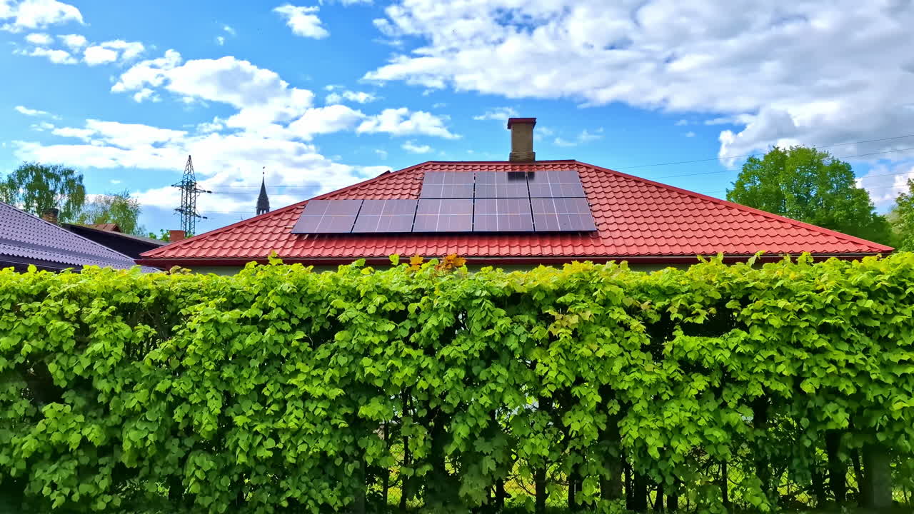 Small residential house with red tile roof and solar panels behind lush green hedge