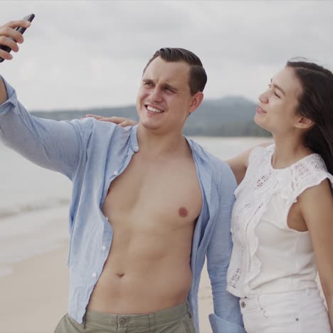 Pleased-people-in-love-making-selfie-on-smartphone-and-smiling-at-exotic-ocean-side