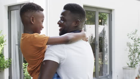 Un-Hombre-Afroamericano-Abraza-A-Un-Niño-Alegre-En-Casa