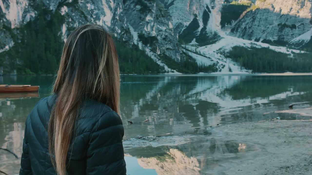Woman with long hair standing by a mountain lake admiring the beautiful alpine landscape